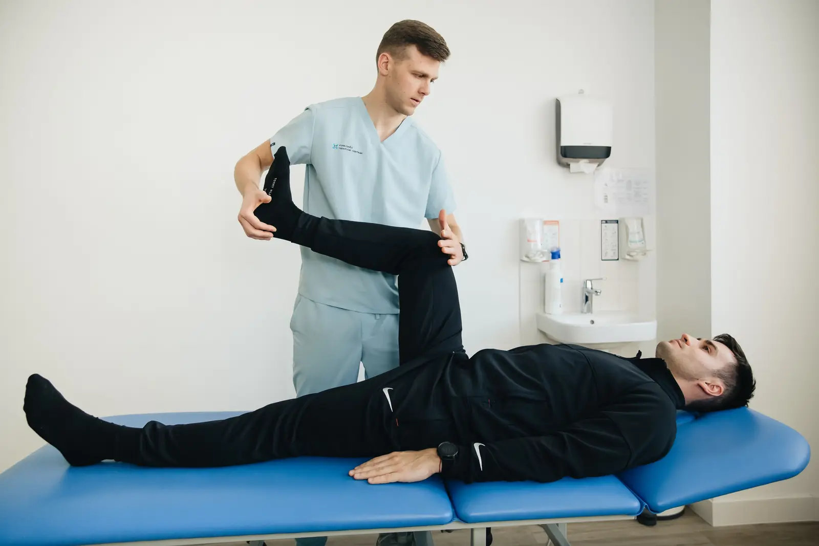 A physiotherapist stretching a patient's leg on a treatment table in a clinic room.