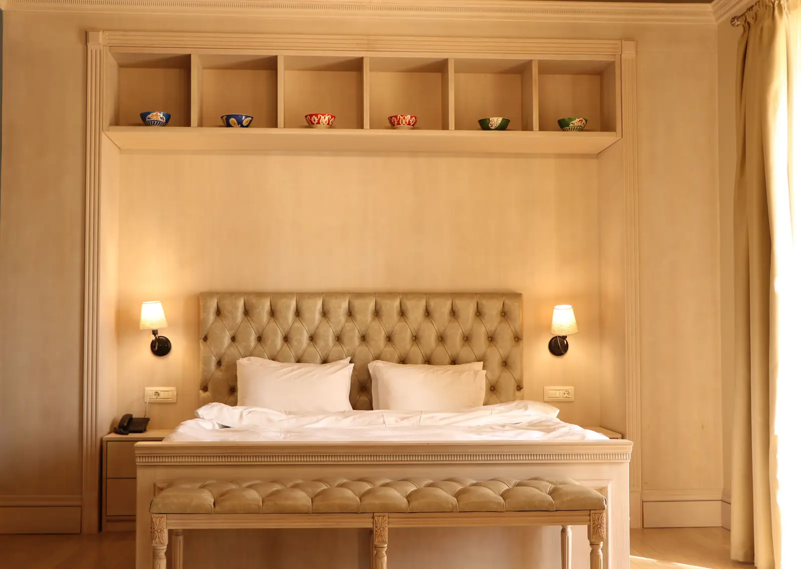 An empty hotel room with the bed made and the bedside lights on, ready for a guest.