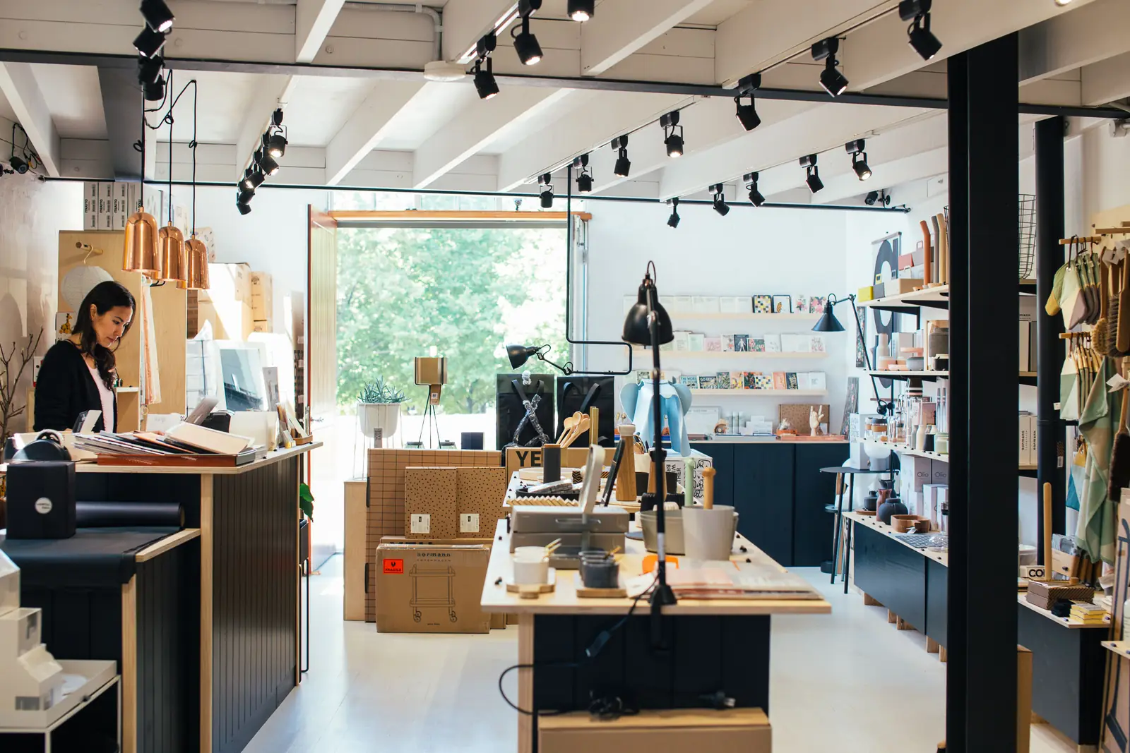 A small independent shop: the owner at the counter, stock on the shelves and parcels packed beside the till.